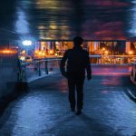 Man walking through dark tunnel towards lighted street.